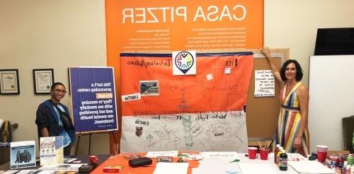 Two CASA employees stand at an info desk with presentation posters